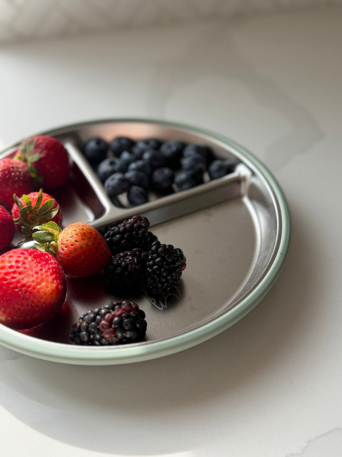 BRAI + CO. divided stainless steel and silicone plate with strawberries, blackberries, and blueberries.